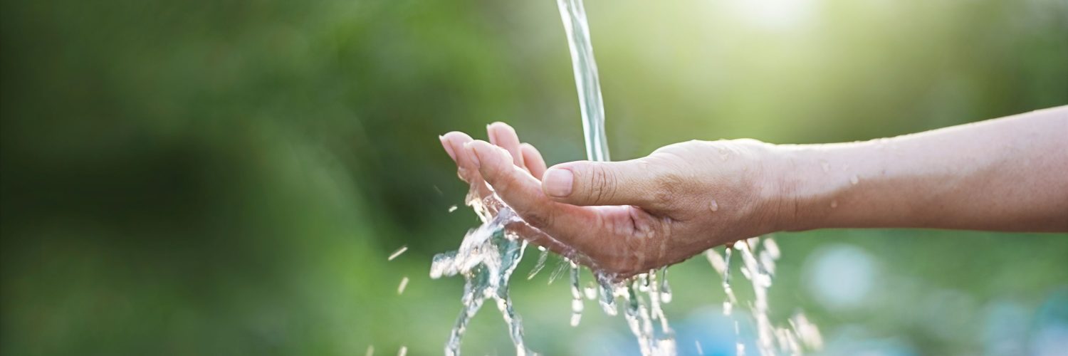 Water pouring in woman hand on nature background, environment issues